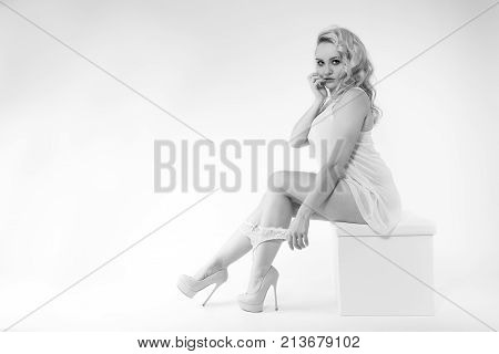 Young woman sitting on a stool in white top high-heels and lingerie