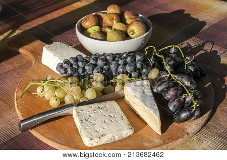 Wooden plateau with fresh grapes figs and types of cheese closeup as homefood background