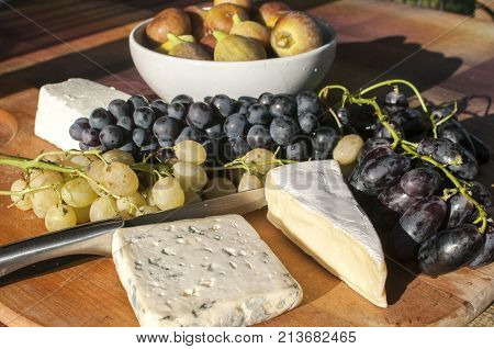Wooden plateau with fresh grapes figs and types of cheese closeup as homefood background