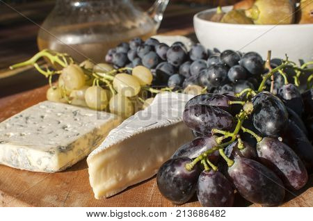 Wooden plateau with fresh grapes figs and types of cheese closeup as homefood background