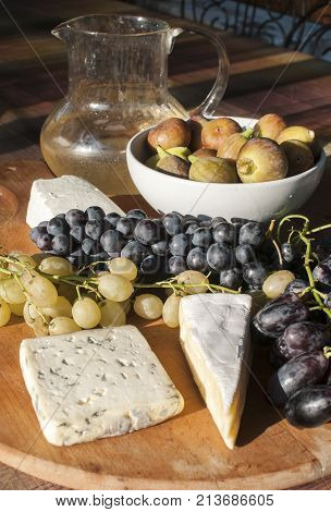 Wooden plateau with fresh grapes figs and types of cheese closeup as homefood background
