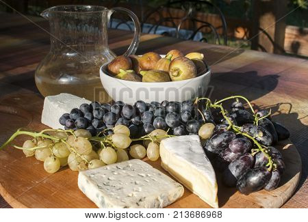 Wooden plateau with fresh grapes figs and types of cheese closeup as homefood background