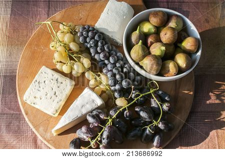 Wooden plateau with fresh grapes figs and types of cheese closeup as homefood background