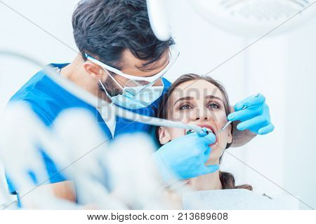Young woman during painless oral treatment in the modern dental clinic led by an experienced dentist