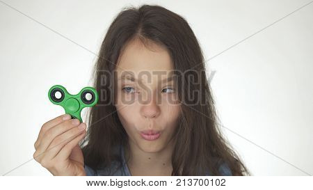 Beautiful cheerful teen girl playing with green fidget spinner on a white background