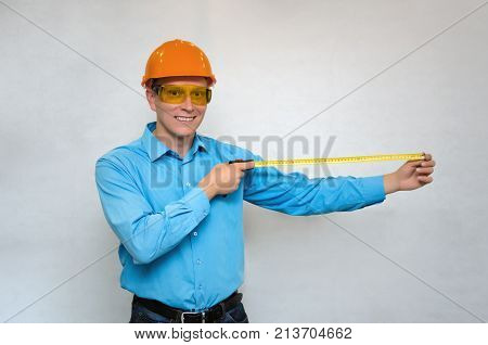 Happy smiling worker in hardhat holding in hands construction roulette and measures copy space behind of him isolated. Engineer takes measurements.