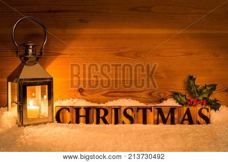 The word Christmas next to lantern with candle inside on a snow and wod background with holly 
