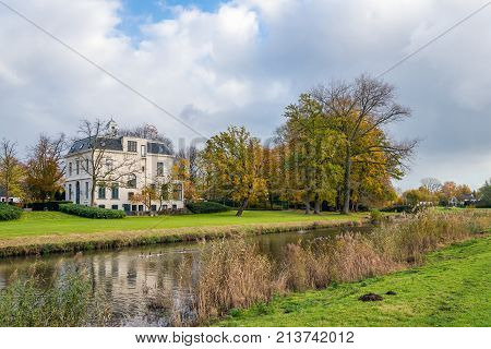 Small river in the Netherlands on a cloudy day in the fall season. The white plastered house was built in 1919 in eclectic style. Now it is a national monument.