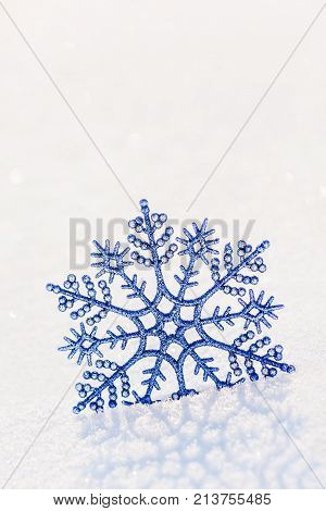 Winter vertical background with shiny decorative blue snowflake on brilliant snow surface in sunset sunlight Merry Christmas and Happy New year concept