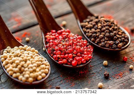 Close up studio shot of assorted peppercorn in spoons on dark background