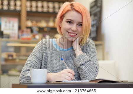 atural light portrait of young attractive smiling student girls schoolgirl at a table in a cafe with a notebook and pen doing home work.