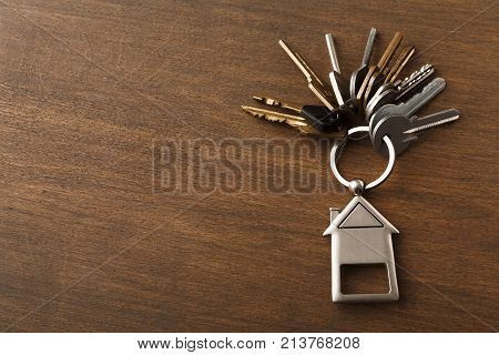 Bunch of keys on a house shaped keychain at wooden table background. Concept for real estate or renting home with copy space, top view
