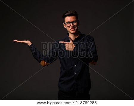 Young jocular man portrait of a confident businessman showing by hands on a black background. Ideal for banners, registration forms, presentation, landings, presenting concept.