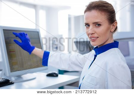 One more step. Portrait of female scientist transferring data from experiment looking straight while holding her hand near the screen