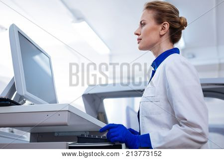 Working hard. Low angle of focused pleasant female scientist staring  at the screen holding hands near the keyboard  standing in the lab