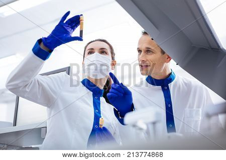 Interesting case. Brunette female scientist holding blood sample and wanting to compare with another one while attractive man scientist pointing with his finger