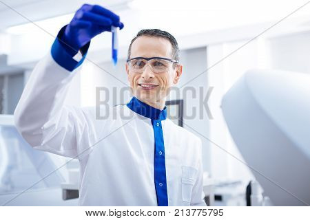 Lets see. Joyfull  determined male researcher jiggling test tube with blue liquid while examining it and standing in the lab