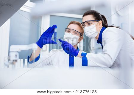 New observation. Pleasant exited young researchers noticing strange reaction in the test tube when one woman holding it and the other pointing at it