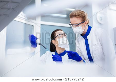 Little mistake. Blond pleasant laboratorian pointing at mistake in the process of checking on AFP conducted by her wondered colleague