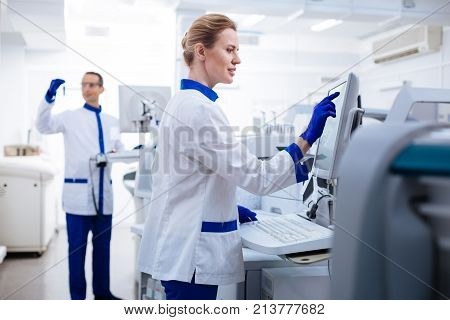 Order in everything. Pensive good looking female researcher   touching the screen and looking at it while standing in the lab