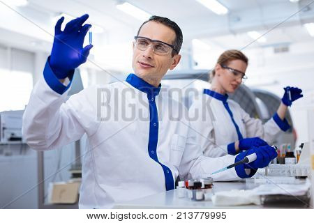Advanced medication.  Kind budding male scientist placing the hand with pipette on the table and holding up the medication sample while wearing lab coat