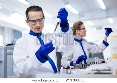 Medical procedure. Interested curious male lab assistant   placing reagent into the glassware with a pipette which located in his hand while looking at liquid attentively
