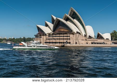 Sydney Australia - March 26 2017: Frontal view of beige-brown Opera House seen off the water with white speed boat in front under blue sky.