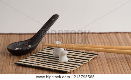 Wooden chopsticks on white porcelan "lion" chopsticks rest.  black porcelan spoon on bamboo mat. White background. Front view. Closeup