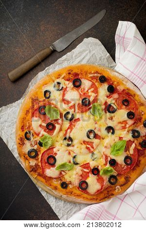 Pizza margarita with tomatoes mazarella and slices of olives on a dark concrete or stone background. Traditional Italian cuisine. Selective focus. Top view.