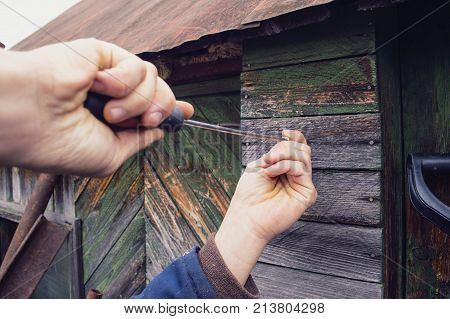 The village man screws a screwdriver into the wooden wall with a long screwdriver