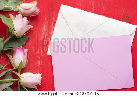 Message card on envelope and roses - Greeting card idea with a pink paper on a closed envelope surrounded by roses on a red wooden background. A concept for mother day valentine day and events.