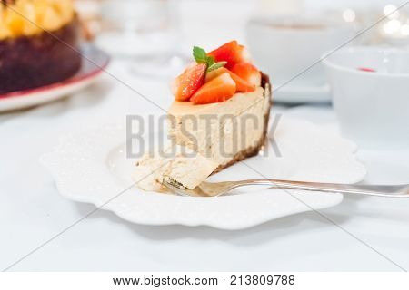Cheesecake with strawberries and mint leaves on a white plate close up