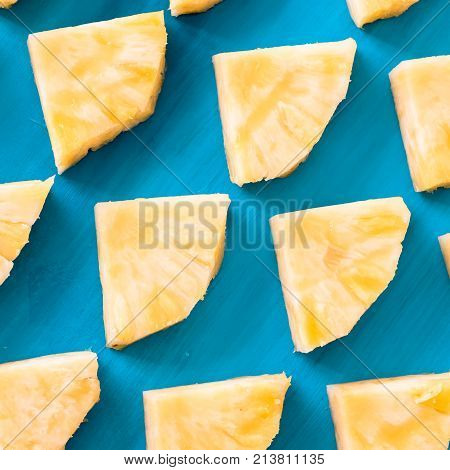 Close up patter of many pieces of yellow pineapple laying on blue wooden table background.
