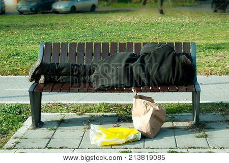 Homelessness Homeless refugee man in black coat sleeps on the bench on the street
