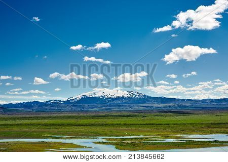 Travel to Iceland. road and river in a bright sunny mountain landscape. Vatna volcano covered with snow and ice on tne background.