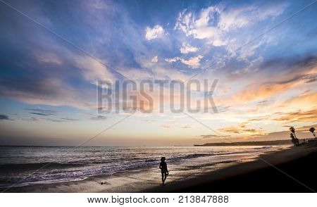 Woman walking along shoreline at sunset with beautiful sky above