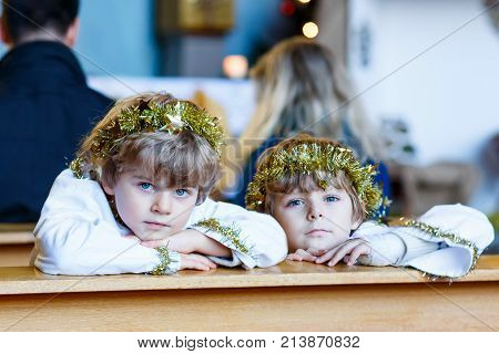 Two beautiful little kis in angel clothes for Christmas story in a church. Happy adorable blond children, boys singing and excited about holiday.