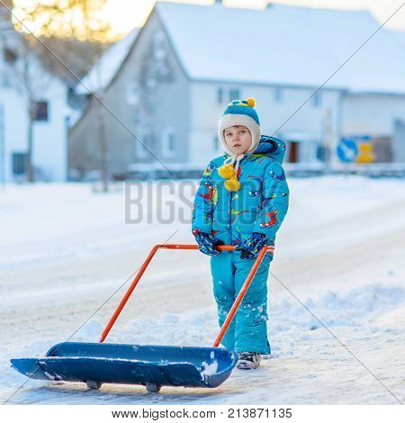 Cute little kid boy in colorful winter clothes having fun with snow shovel, outdoors during snowfall. Active outdoors leisure with children in winter. Happy child with warm hat, hand gloves, winter fashion