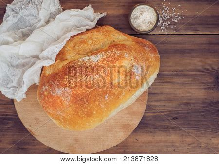 Fresh loaf of bread covered with a white cloth next to the sprinkle salt on a wooden table from the old boards. The view from the top, the background for menu, ads, poster with place for your text.