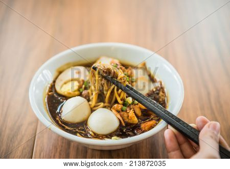 Soft focus hand with Chinese chopsticks eating noodle a famous Malaysia Loh Mee.