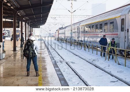 Zagreb Croatia: January 7 2016: Girl waiting at the platform of the trainstation Zagreb along snowed trainrails and workers passing by standing train