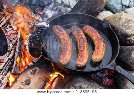 Cooking Sausages In Cast Iron Skillet On Campfire While Camping. Good And Positive Campfire Food.