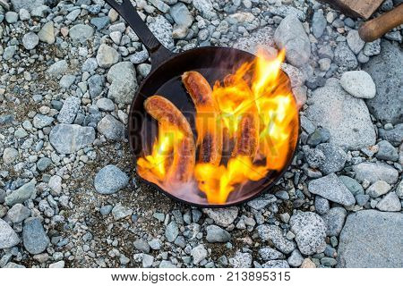 Cooking Sausages In Cast Iron Skillet On Campfire While Camping. Good And Positive Campfire Food.