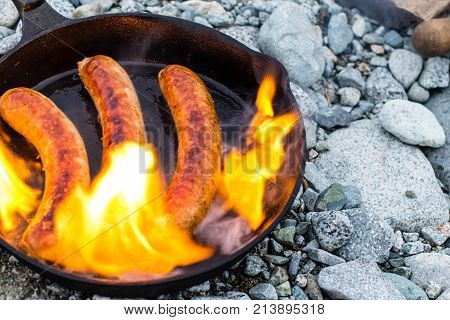 Cooking Sausages In Cast Iron Skillet On Campfire While Camping. Good And Positive Campfire Food.