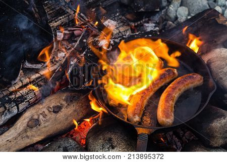 Cooking Sausages In Cast Iron Skillet On Campfire While Camping. Good And Positive Campfire Food.