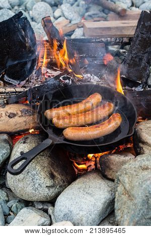 Cooking Sausages In Cast Iron Skillet On Campfire While Camping. Good And Positive Campfire Food.