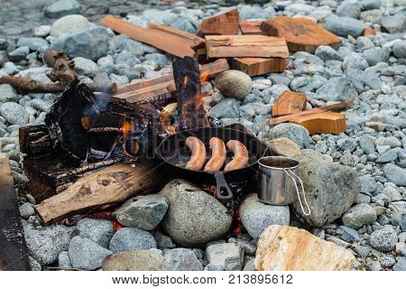 Cooking Sausages In Cast Iron Skillet On Campfire While Camping. Good And Positive Campfire Food.