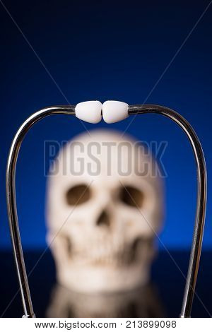 Stethoscope i focus and blurry skull isolated on black blue background