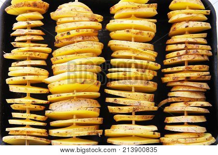 Raw yellow potatoes in a peel, cut into slices. Pieces are strung on wooden skewers and prepared for baking.