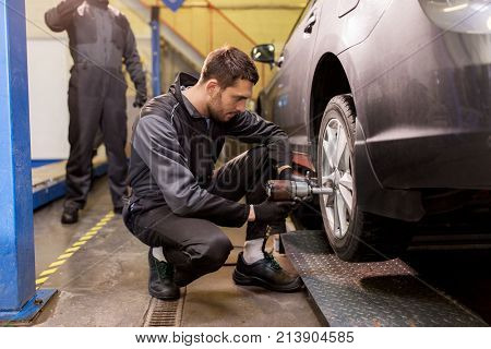 car service, repair, maintenance and people concept - auto mechanic man with electric screwdriver changing tire at workshop